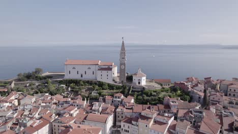 Video-with-drone-from-overhead-shot-backwards-over-the-city-of-Piran-in-Slovenia,-starting-with-the-Church-as-the-main-one-and-ending-from-overhead-at-the-marina-passing-through-the-central-square