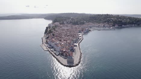 Video-with-a-bird's-eye-view-of-the-lighthouse-of-the-city-of-Piran-in-Slovenia,-with-people-walking-and-the-church-in-the-background