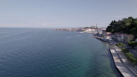 Frontal-drone-video-advancing-over-the-coast-of-the-city-of-Piran-in-Slovenia-with-the-seaport-and-the-church-in-the-background,-the-sky-is-clear-and-the-flight-is-a-few-meters-above-sea-level