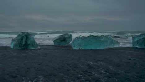 Panning-shot-of-giant-Icebergs-at-Diamond-Beach-during-cloudy-grey-sky-in-Iceland-and-wavy-ocean