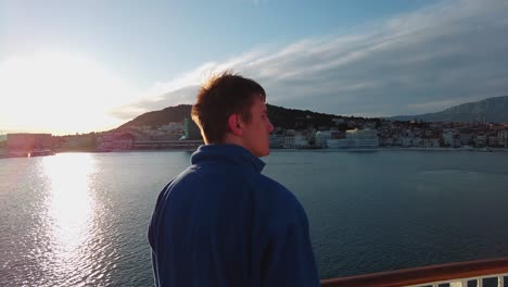 A-young,-attractive-man-with-dark-brown-hair-and-a-blue-jacket-looking-at-distant-objects-from-the-ferry-boat-which-is-sailing-from-Split-to-island-Vis-in-Croatia,-in-the-Adriatic-Sea-4K-UHD
