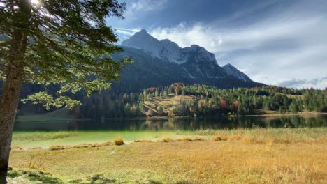 Toma-Panorámica-Del-Lago-Ferchen-Con-El-Bosque-Dorado-De-Otoño-Y-La-Montaña-Grünkopf-Al-Fondo,-Muy-Cerca-De-La-Ciudad-Bávara-De-Mittenwald-En-Alemania