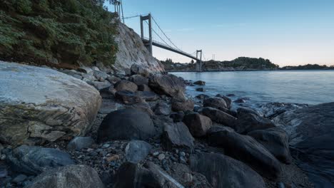 Day-to-night-time-lapse-transition-view-of-Herdla-bridge,-Askoy,-Norway-low-angle-view-of-water,-rocks-and-sky