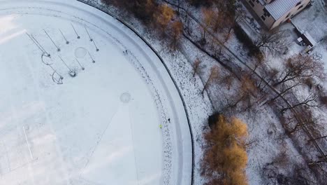 Group-of-runners-on-snowy-running-track,-winter-running-aerial-shot