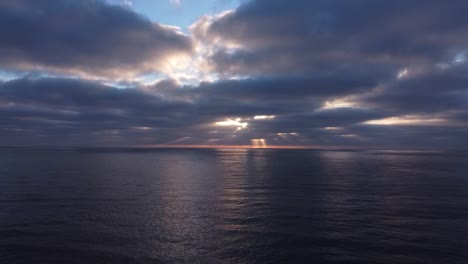 Drone-view-of-sun-rays-peaking-through-thick-dark-clouds-over-the-ocean-in-the-evening