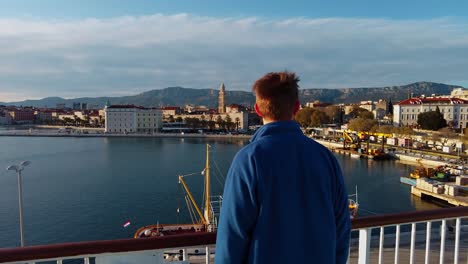 A-young-man-wearing-a-blue-jacket-with-brown-hair-standing-alone-during-the-Covid-pandemic-on-the-deck-of-a-ferry-boat-which-is-sailing-from-Split-to-island-Vis-in-Croatia,-in-the-Adriatic-Sea-4K-UHD