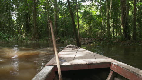 A-wooden-boat-winds-down-a-narrow-stretch-of-the-Amazon-river-surrounded-by-jungle-on-a-sunny-day
