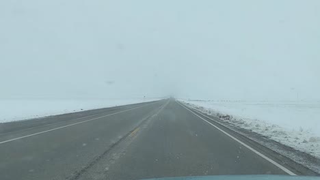 Winter-driving-along-a-long-road-with-little-traffic,-in-an-icy-landscape,-foggy-weather-and-falling-snow