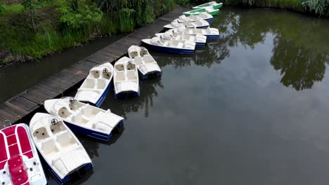 Pedal-Boats-Moored-In-Row-By-The-Wooden-Jetty-On-The-Lakeside-At-Daytime