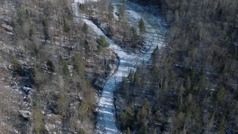 Gefrorener-Fluss-Durch-Waldbäume-Im-Berg-An-Einem-Sonnigen-Wintertag-In-Quebec,-Kanada