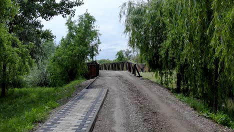 Dirt-Road-With-Willow-Trees-Towards-The-Wooden-Bridge