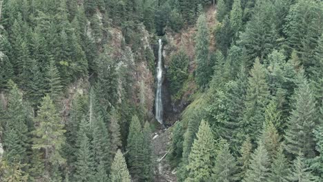 Scenic-View-Of-Tall-Waterfall-Pouring-Out-Of-Narrow-Gorge-With-Lush-Green-Pine-Trees-In-British-Columbia,-Canada