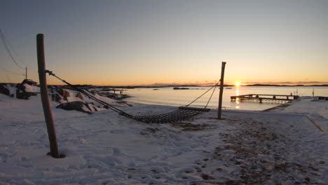 4k-Close-up-shot-of-a-wooden-hammock-by-a-snowy-beach-on-a-winter-day-during-sunset-in-Sweden