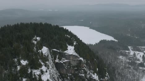 Mann-Auf-Dem-Gipfel-Des-Felsigen-Berges-Im-Schnee-Mit-Kiefernwald-Im-Winter-In-Quebec,-Kanada