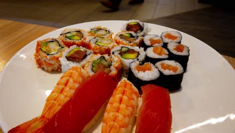 Wild-salmon-and-tuna-rotating-on-an-assorted-plate-closeup-on-a-white-plate-rotating-at-a-Chinese-Japanese-Buffet-All-you-can-eat-as-people-head-into-their-designated-seating-area-in-the-background