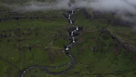 Toma-Aérea-Ascendente-De-La-Cascada-Klifbrekkufossar-Que-Fluye-Entre-Enormes-Acantilados-En-Islandia