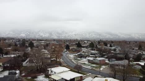 An-aerial-drone-shot-tracking-backwards-over-a-residential-area,-in-the-distance-a-spectacular-view-of-the-Wasatch-Mountains-covered-in-snow-on-a-cold-gloomy-winter’s-day,-Layton,-Utah