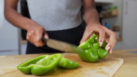Dark-skinned-woman-cutting-a-green-bell-pepper-into-pieces-on-a-wooden-cutting-board