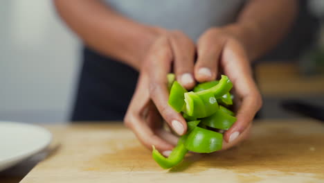 Dark-skinned-woman's-hands-placing-chopped-green-peppers-next-to-the-rest-of-the-vegetables-on-a-plate
