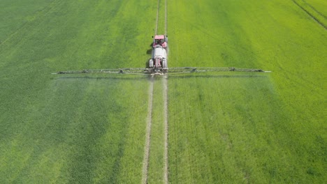 Aerial-following-shot-of-the-agricultural-sprayer-spraying-insecticide-to-the-green-field-on-spring