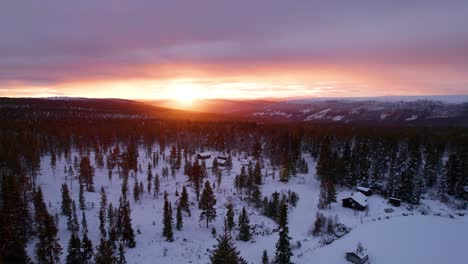 Sunset-in-a-winter-mountain-forest-landscape-with-wooden-cabins