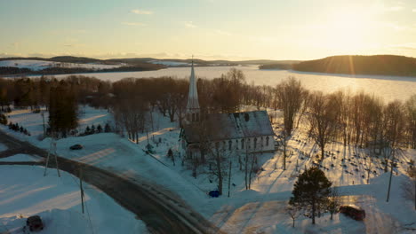 Beautiful-drone-view-of-a-winter-sunset-over-a-snow-covered-small-town-church