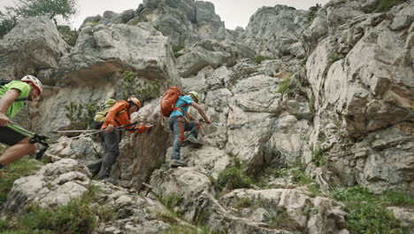 Hikers-wearing-backpacks-and-helmets-climbing-up-a-steep-part-of-a-climb-on-a-mountain