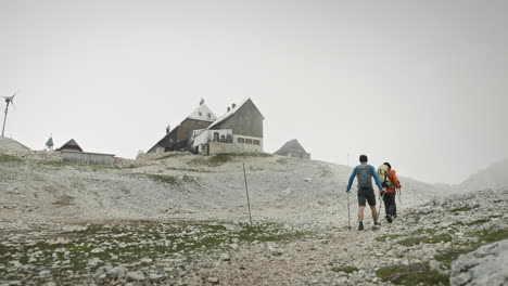 Hikers-with-backpacks-and-hiking-poles-walkinh-towards-the-mountain-cottage