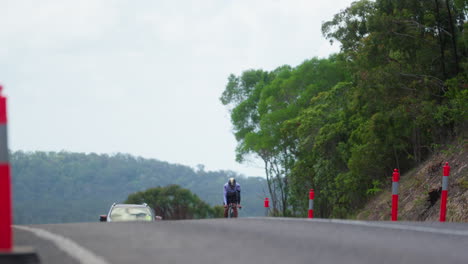 Professional-Cyclist-Riding-Bike-On-Shared-Road-With-Car-Driving-Behind,-Up-Hill,-4K