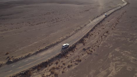 Cars-driving-on-dusty-desert-road-in-stunning-sunset