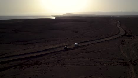 Aerial-view-of-cars-driving-the-dusty-road-on-the-desert-during-late-sunset