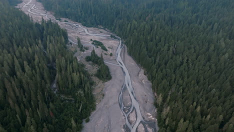 Slow-aerial-footage-of-a-riverbed-that-is-in-between-a-forest-of-evergreen-trees-in-the-Cascade-Mountains