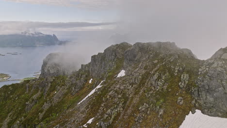 Djevelporten-Norway-Aerial-v6-high-altitude-drone-flyover-mountain-ridges,-fly-through-thick-layer-of-fog-reveals-svolvær-airport-and-beautiful-fjord-landscape---Shot-with-Mavic-3-Cine---June-2022