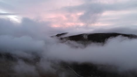 Colorful-cloudy-sunset-with-the-mountains-peaking-from-the-clouds-drone-shot