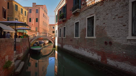 Un-Barco-En-Un-Canal-En-Venecia,-Italia-Con-Casas-Antiguas-Y-Una-Iglesia-Catedral-Cerca-De-San-Marco-Y-El-Puente-De-Rialto