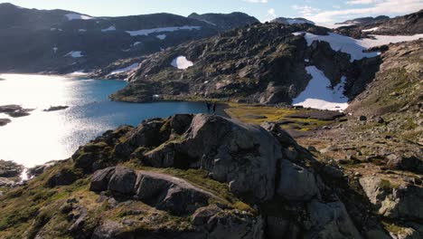People-standing-on-top-of-the-hill-above-a-natural-lake-in-the-national-park-Hadrangervidda-in-Norway-drone-shot