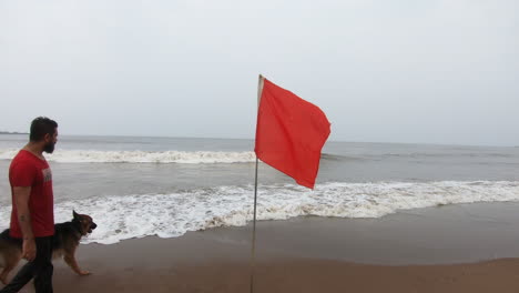 German-shepherd-dog-on-the-beach-playing-with-his-owner-near-red-flag-warning-sign-|-Red-flag-warning-high-alert-on-beach