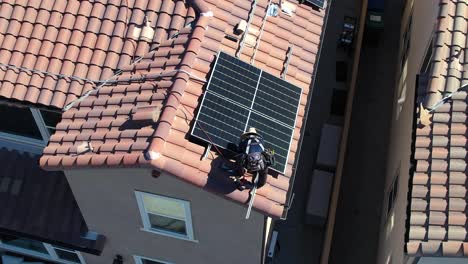 Static-drone-shot-of-installer-on-home-roof,-working-on-new-solar-panels,-clean-energy