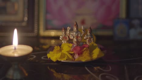 Pequeña-Estatua-De-Deidades-Hinduistas-Con-Flores-Como-Ofrendas,-Vela-Encendida-En-Primer-Plano