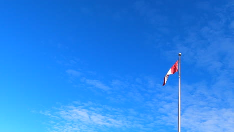Canadian-National-Flag-on-Pole-Waving-Swaying,-Blue-Sky-in-Background,-Low-Angle-Establishing-View
