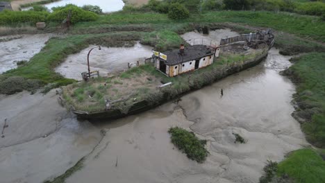 Wooden-Lighterboat-stranded-and-stuck-in-the-marsh-at-Wat-Tyler-Country-Park,-cloudy-Basildon,-UK---Aerial-view