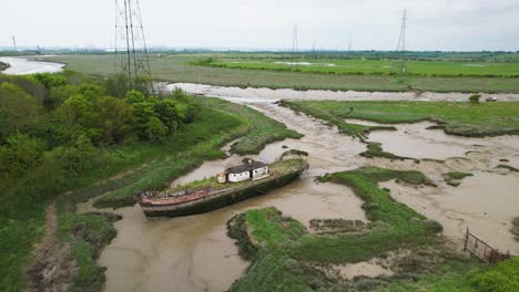 Aerial-view-over-a-abandoned-boat,-in-Wat-Tyler-Country-Park,-cloudy-Basildon,-UK---tilt,-drone-shot