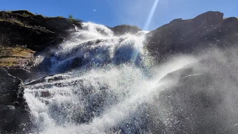 Powerful-splashing-waterful-in-beautiful-sunlight-at-Vikafjell-mountain-in-Norway---Spring-with-blue-sky-and-camera-almost-inside-the-lower-part-of-waterfall---Low-angle-looking-up-at-waterfall