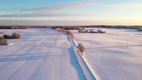 Romantic-sunset-over-pure-white-snowy-landscape-during-snowfall,-aerial-view