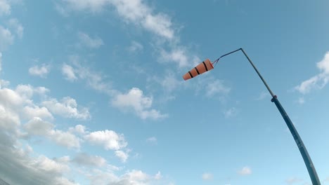 Looking-up-at-slow-motion-striped-airport-windsock-blowing-against-blue-cloudy-sky