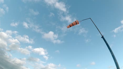 Slow-motion-striped-airport-windsock-blowing-against-blue-cloudy-sky-looking-up
