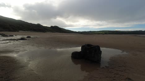 Time-lapse-shimmering-breezy-beach-rock-pool-clouds-passing-above-woodland-coastline-dolly-right