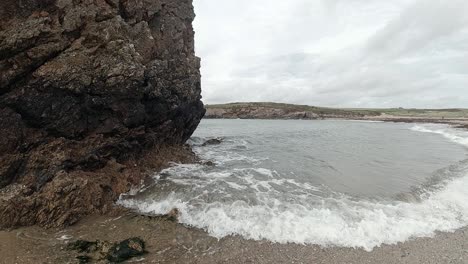 Slow-motion-ocean-waves-splashing-around-large-rock-shoreline-Anglesey