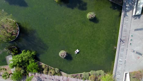 Topdown-view-along-lagoon-with-pedal-boat-cruise-on-water-surface-the-Quinta-Normal-park,-Santiago