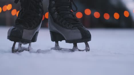 Close-up-of-person-walking-on-ice-skates-on-ice,-blurred-lights-in-background